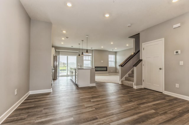 unfurnished living room with baseboards, recessed lighting, stairs, and dark wood-style flooring