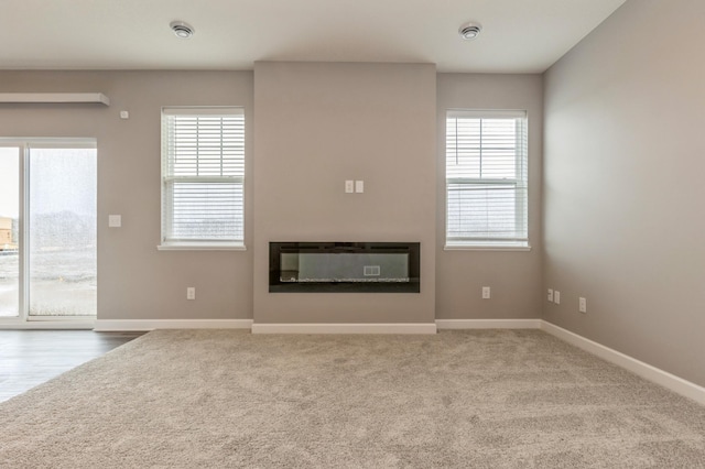unfurnished living room with a glass covered fireplace, baseboards, and carpet