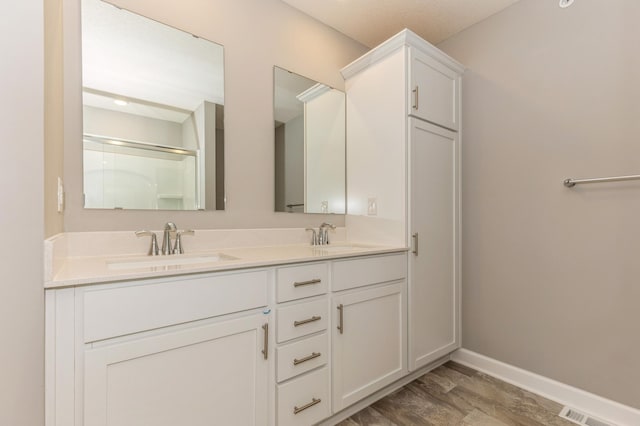 bathroom with wood finished floors, baseboards, double vanity, and a shower with shower door