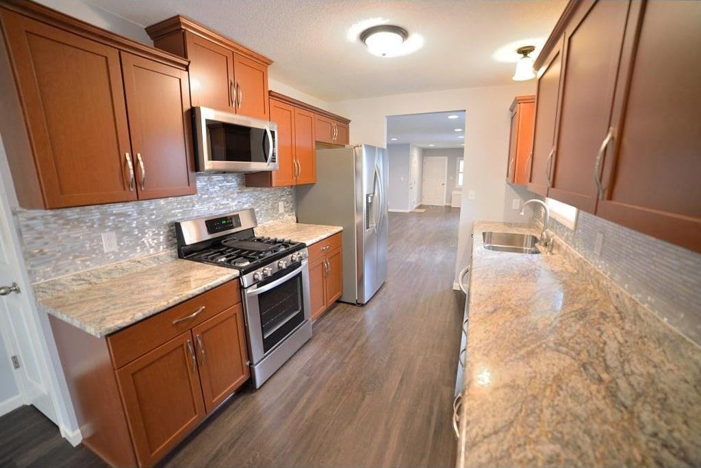 kitchen with appliances with stainless steel finishes, a sink, tasteful backsplash, dark wood-style floors, and brown cabinetry