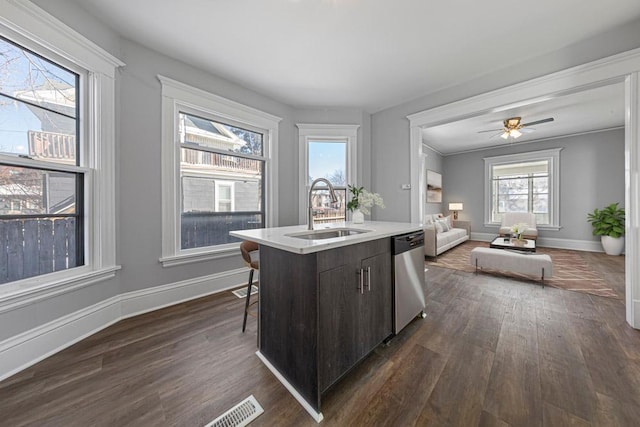 kitchen with a sink, stainless steel dishwasher, a kitchen island with sink, dark wood-style flooring, and baseboards