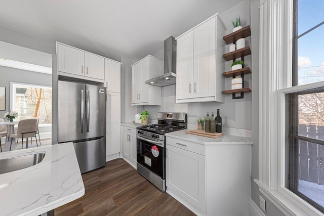 kitchen featuring stainless steel appliances, wall chimney range hood, open shelves, light stone counters, and white cabinetry