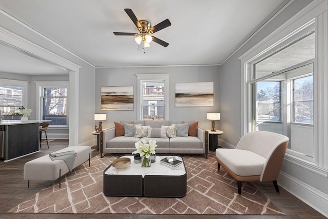 living area with baseboards, ornamental molding, ceiling fan, and wood finished floors