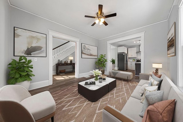 living area featuring a ceiling fan, stairway, baseboards, wood finished floors, and ornamental molding
