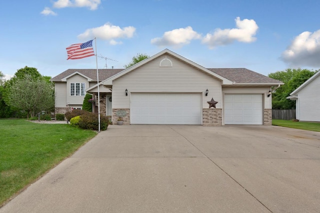 tri-level home with an attached garage, concrete driveway, a front lawn, a shingled roof, and stone siding