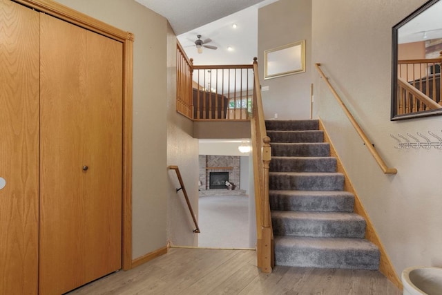 staircase featuring wood finished floors, ceiling fan, a fireplace, and baseboards