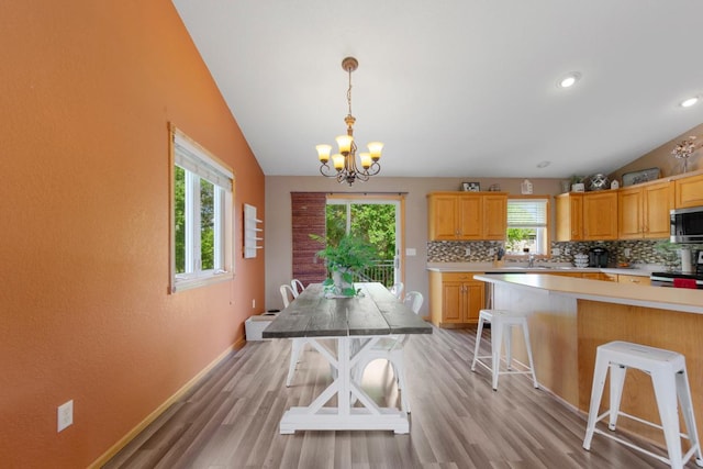 dining area with a chandelier, vaulted ceiling, light wood-type flooring, recessed lighting, and baseboards