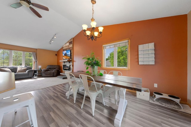 dining area with lofted ceiling, light wood-type flooring, a chandelier, ceiling fan, and a fireplace