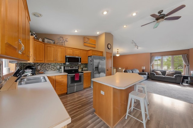 kitchen with appliances with stainless steel finishes, a sink, open floor plan, a kitchen island, and light countertops