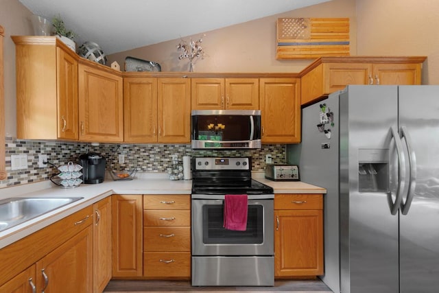 kitchen featuring appliances with stainless steel finishes, wood finished floors, vaulted ceiling, light countertops, and tasteful backsplash