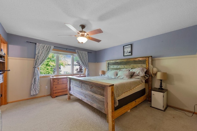 bedroom with light carpet, a textured ceiling, a ceiling fan, and baseboards