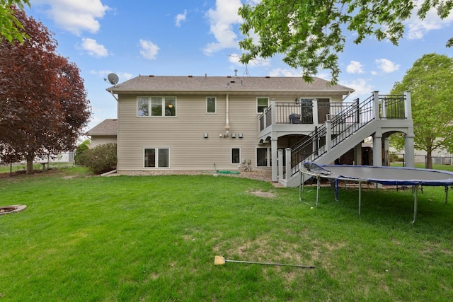 rear view of house featuring stairway, a trampoline, a yard, and a deck