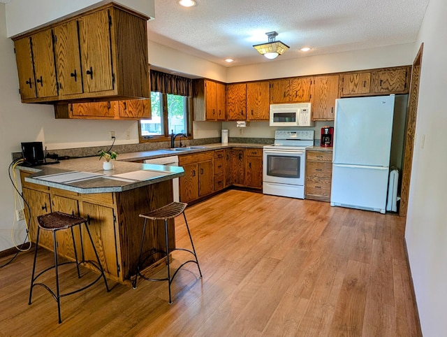 1401 5th St, Montevideo, MN 56265 - kitchen with white appliances, a peninsula, brown cabinets, a sink, and light wood-style flooring