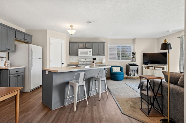 kitchen with white appliances, dark wood-type flooring, gray cabinets, a kitchen island with sink, and a textured ceiling