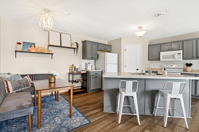kitchen with white appliances, gray cabinetry, dark wood-type flooring, light countertops, and a breakfast bar area