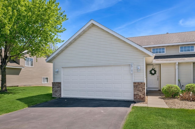 view of front of house featuring asphalt driveway, brick siding, a front lawn, a garage, and a shingled roof