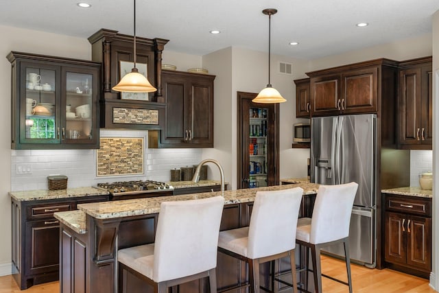 855 Elins Lake Rd SE, Cambridge, MN 55008 - kitchen with appliances with stainless steel finishes, light wood-style floors, dark brown cabinetry, decorative backsplash, and a kitchen bar