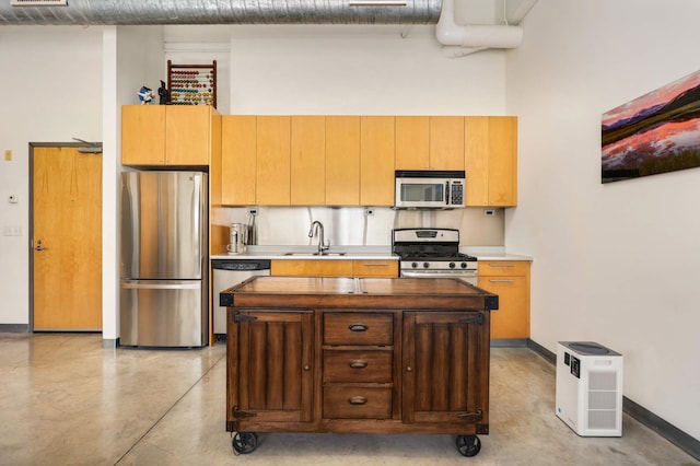kitchen with appliances with stainless steel finishes, finished concrete floors, a sink, and a center island
