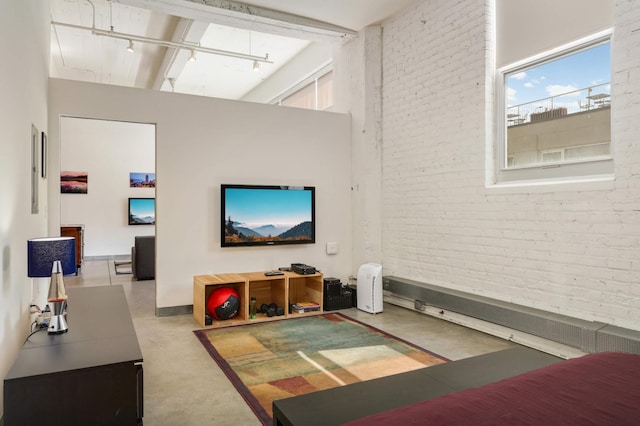 living room with finished concrete floors, a towering ceiling, brick wall, and track lighting
