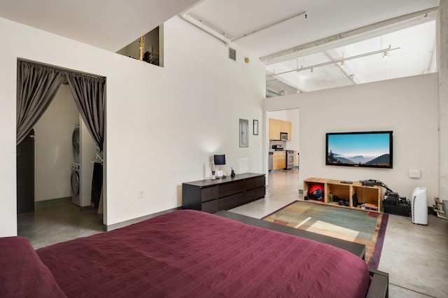 bedroom with stacked washer / dryer, finished concrete floors, track lighting, and a high ceiling