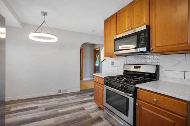4528 6th St NE, Columbia Heights, MN 55421 - kitchen featuring appliances with stainless steel finishes, arched walkways, light wood-style floors, baseboards, and brown cabinetry