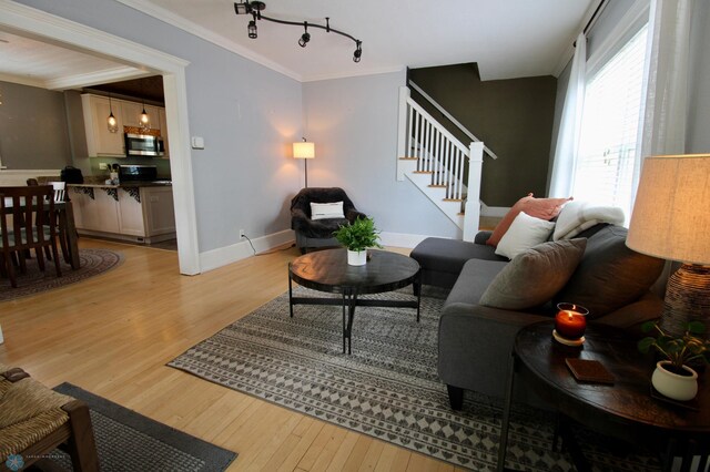 living area with stairway, light wood-style flooring, crown molding, baseboards, and rail lighting