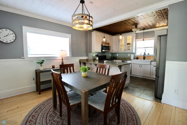 dining area with light wood-type flooring, baseboards, a chandelier, and crown molding