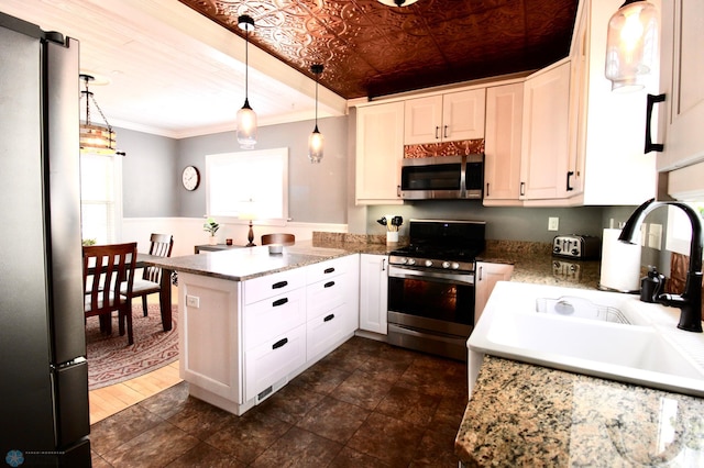 kitchen featuring stainless steel appliances, a peninsula, ornamental molding, white cabinets, and hanging light fixtures
