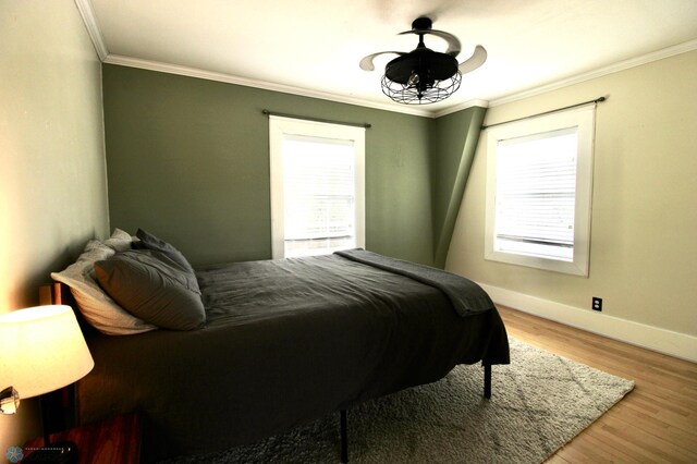 bedroom with multiple windows, ornamental molding, wood finished floors, and baseboards