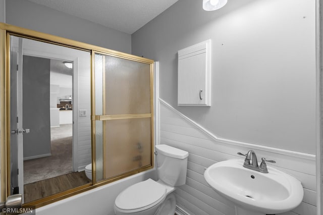 230 8th St NW, Elk River, MN 55330 - bathroom featuring toilet, a sink, wood finished floors, shower / bath combination with glass door, and a textured ceiling
