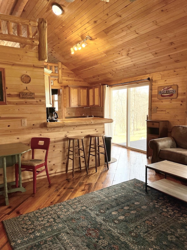 kitchen with vaulted ceiling, wooden walls, light wood-style flooring, a breakfast bar, and wooden ceiling