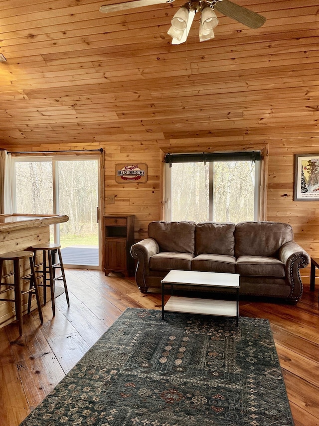 living area with ceiling fan, healthy amount of natural light, wood walls, and hardwood / wood-style flooring