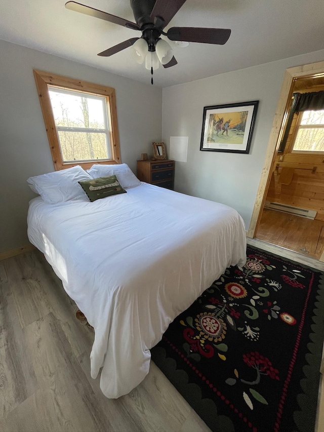 bedroom with wood finished floors, a ceiling fan, baseboards, and baseboard heating