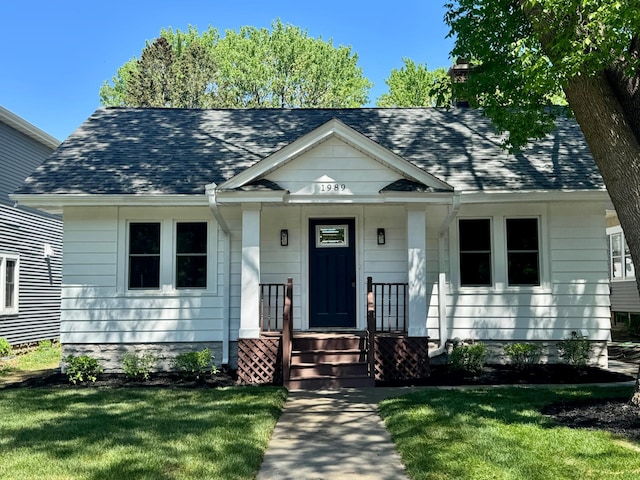 bungalow with a shingled roof, a front yard, covered porch, and a chimney
