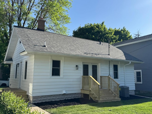 view of front facade with central AC, a chimney, roof with shingles, and a front lawn