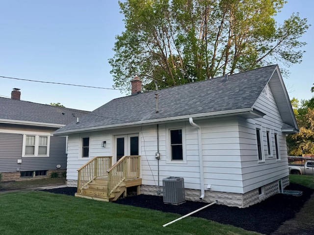 back of house featuring central AC, a yard, roof with shingles, and a chimney