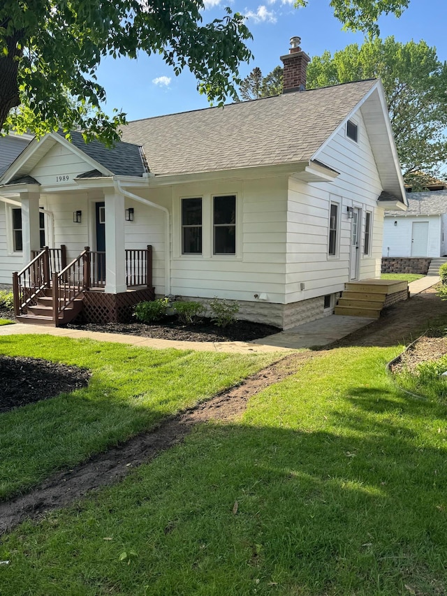 view of front of home with roof with shingles, a chimney, a front yard, and a porch