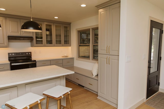 kitchen with electric range, under cabinet range hood, light wood-type flooring, recessed lighting, and glass insert cabinets