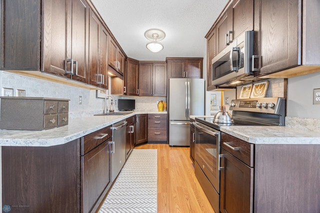 kitchen with stainless steel appliances, a sink, light wood finished floors, tasteful backsplash, and light countertops
