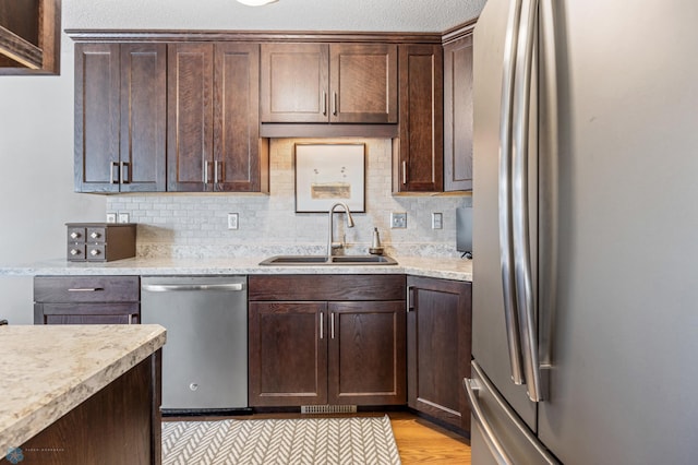 kitchen featuring stainless steel appliances, a sink, dark brown cabinetry, and backsplash