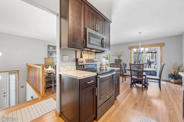 kitchen with appliances with stainless steel finishes, dark brown cabinetry, light countertops, light wood-style flooring, and a chandelier