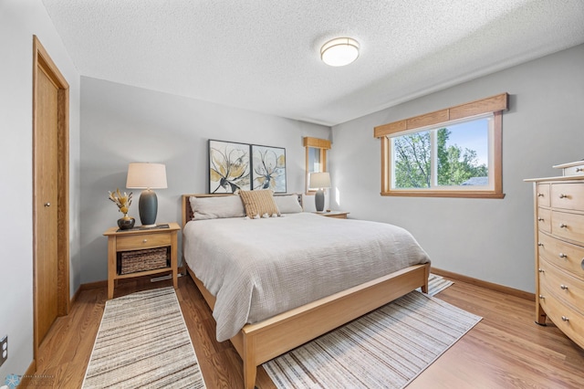 bedroom featuring a textured ceiling, light wood-type flooring, and baseboards