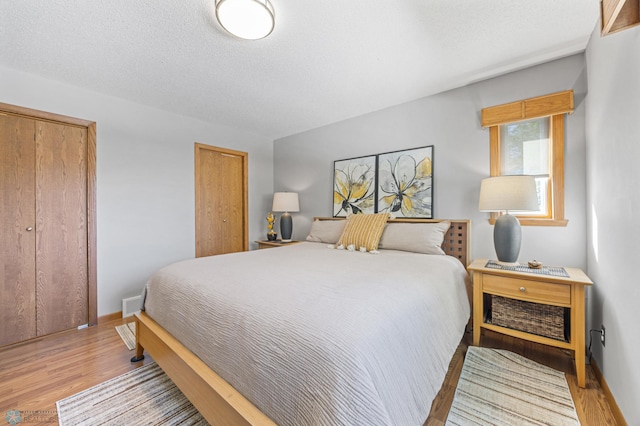bedroom featuring light wood-type flooring, baseboards, two closets, and a textured ceiling