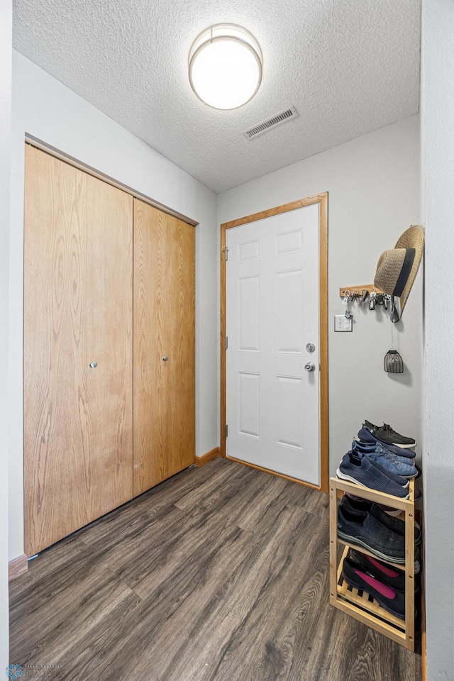 foyer entrance with dark wood-style flooring, a textured ceiling, and baseboards