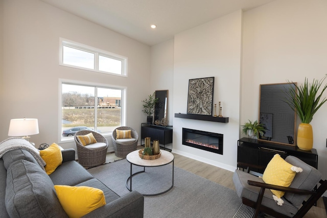 living room with a glass covered fireplace, wood finished floors, a high ceiling, recessed lighting, and baseboards