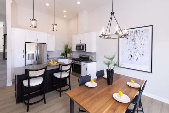 dining space with a chandelier, light wood-type flooring, a towering ceiling, recessed lighting, and baseboards