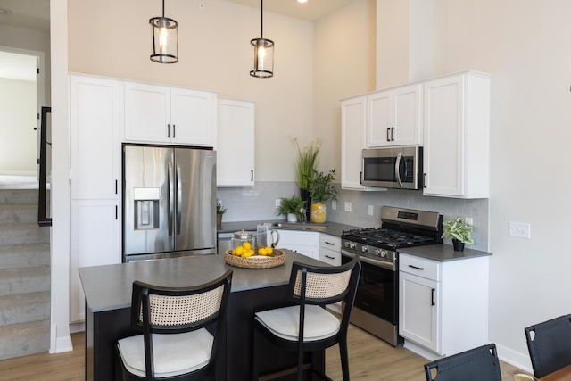 kitchen with appliances with stainless steel finishes, dark countertops, a towering ceiling, light wood finished floors, and white cabinetry