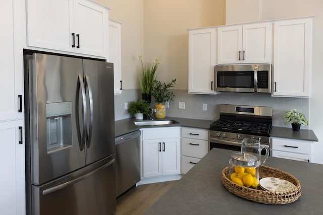kitchen featuring stainless steel appliances, dark countertops, a sink, white cabinets, and tasteful backsplash