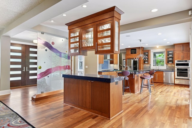154 Babcock Ln, Wayzata, MN 55391 - kitchen featuring appliances with stainless steel finishes, brown cabinets, light wood-style flooring, a kitchen bar, and a kitchen island
