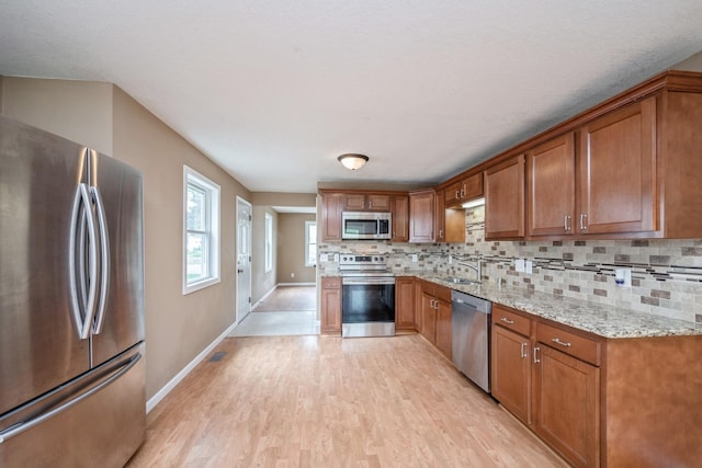 5921 Xerxes Ave S, Minneapolis, MN 55410 - kitchen with stainless steel appliances, brown cabinetry, light wood finished floors, decorative backsplash, and light stone counters
